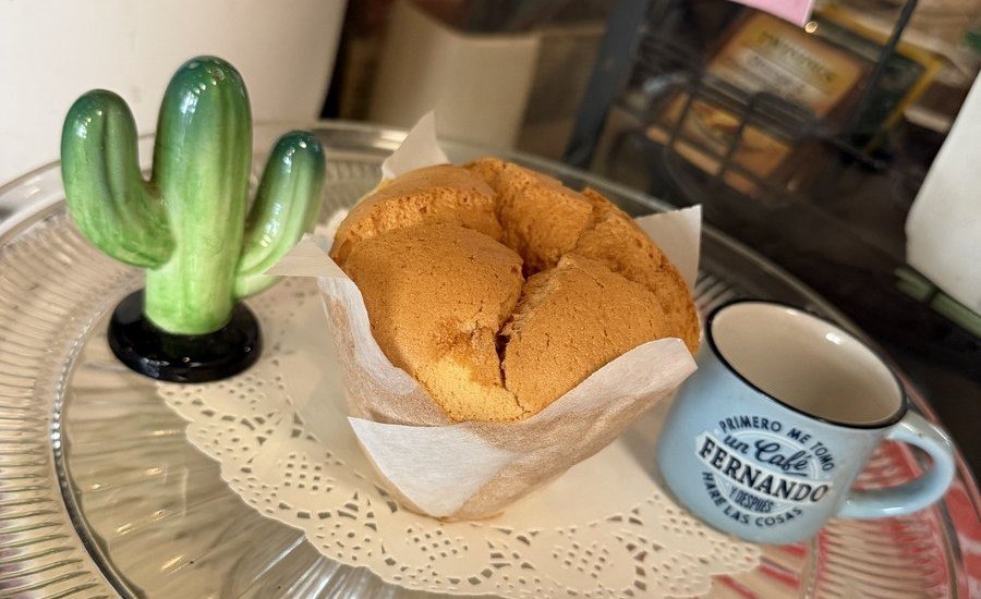 A spongie cake served on a glass cake stand alongside coffee